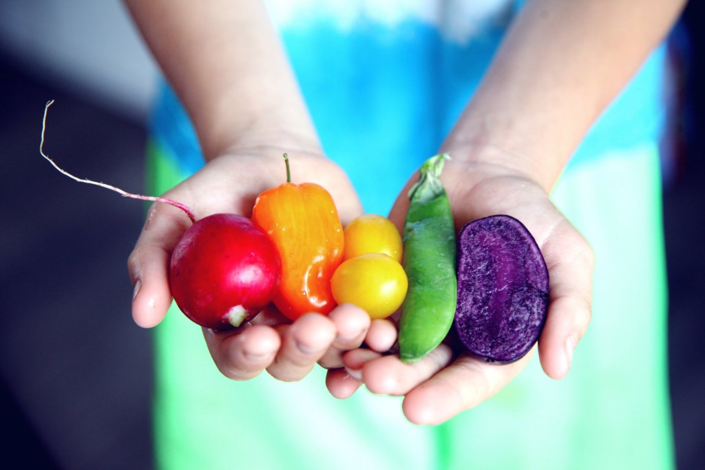 Assortment of fresh fruits and vegetables including apples, oranges, strawberries, spinach, tomatoes, carrots and bell peppers in a wooden basket on a rustic wooden table