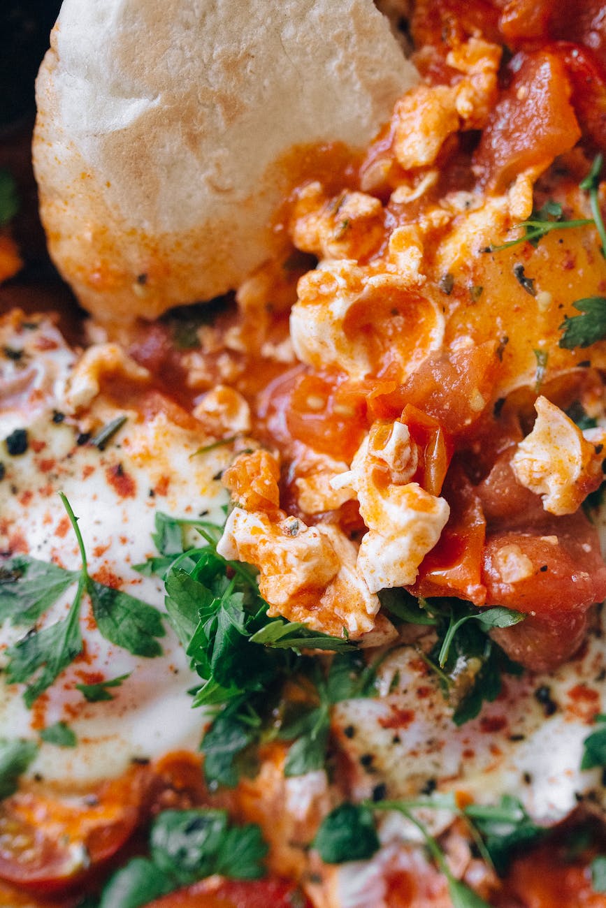 A bowl of homemade hummus garnished with olive oil, paprika, and fresh herbs, served with warm pita bread and colorful vegetable sticks.